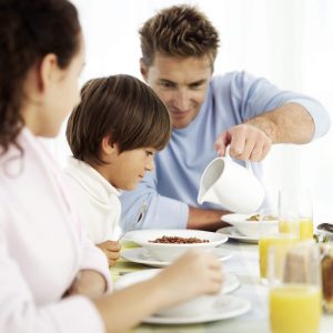 Young Father Pouring Milk into Bowl of Cereal for Young Boy (6-8)