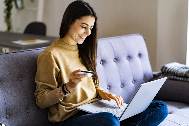 Young Woman With Credit Card Shopping Over Laptop While Sitting At Home